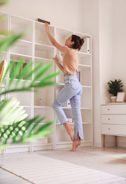 Jeune femme pieds nus prenant livre de l'étagère à la maison - Photo, image