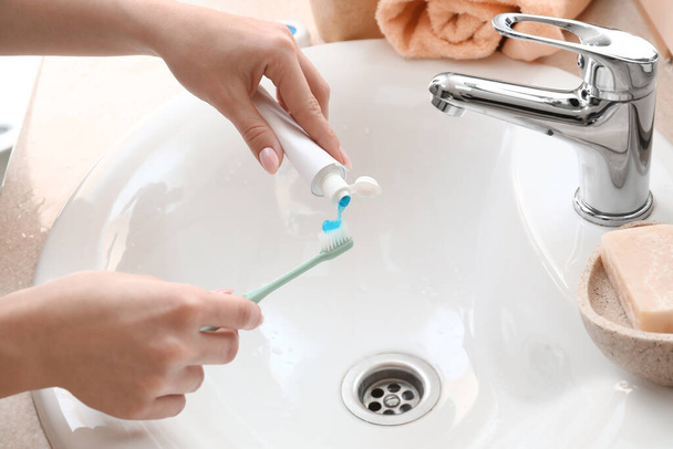 Kobieta nakładająca pastę do zębów na szczoteczkę w pobliżu zlewu w łazience, zbliżenie - Zdjęcie, obraz