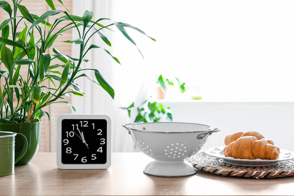Clock, colander and plate with croissants on counter in kitchen - Photo, Image