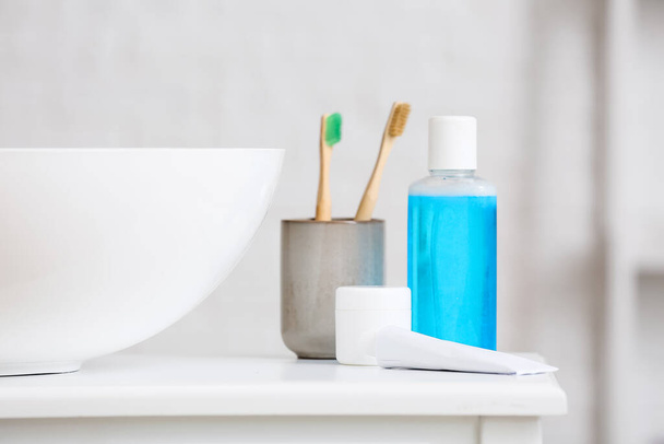 Halter mit Zahnbürsten und Produkten zur Mundhygiene auf einem Tisch in der Nähe des Waschbeckens - Foto, Bild