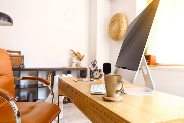 Современный компьютер, микрофон и чашка на столе в светлом помещении, крупный план - Фото, изображение