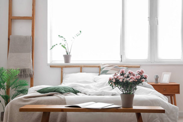 Hermosas flores begonia, portátil y revista en la mesa cerca de la cómoda cama en la sala de luz - Foto, Imagen