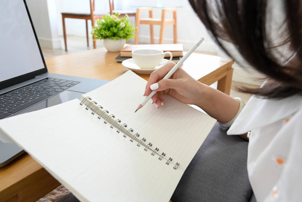 Close-up imagem, estudante universitário feminino escrevendo seu dever de casa em espiral notebook em seu espaço de trabalho. - Foto, Imagem