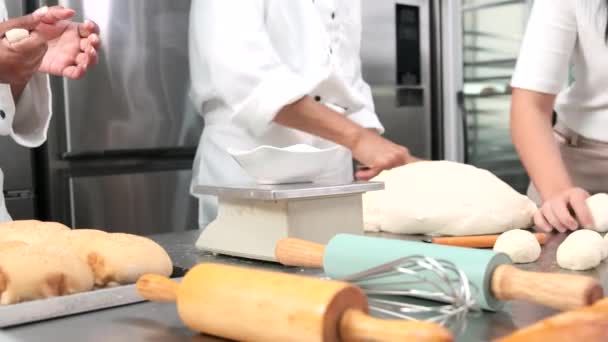 Close-up van de hand chef-koks in witte kok uniformen en schorten zijn kneden rauw deeg deeg, het bereiden van brood, gebak, gebak, en verse bakkerij voedsel, bakken in de oven in roestvrij stalen keuken van restaurant. - Video