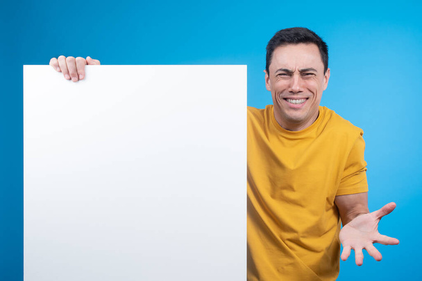 Uomo sorridente confuso che mostra banner in bianco per pubblicità - Foto, immagini