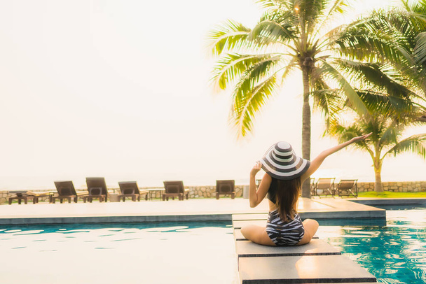 Πορτρέτο όμορφη νεαρή Ασιάτισσα γυναίκα χαλαρώστε γύρω από εξωτερική πισίνα στο θέρετρο του ξενοδοχείου με φοίνικα στο ηλιοβασίλεμα ή την ανατολή του ηλίου για διακοπές αναψυχής - Φωτογραφία, εικόνα