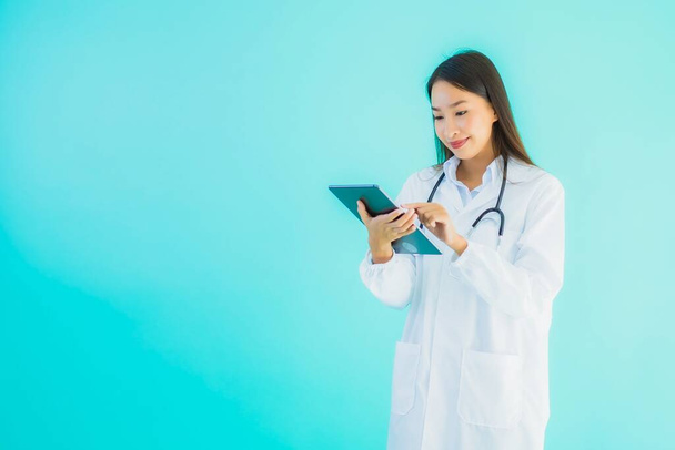 Portrait beautiful young asian doctor woman with stethoscope and smart tablet for use in hospital and clinic on blue isolated background - Zdjęcie, obraz