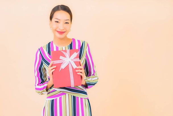 Портрет красива молода азіатка з червоною подарунковою коробкою на кольоровому фоні
 - Фото, зображення