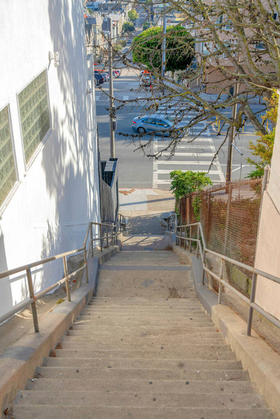 Venkovní schodiště v blízkosti boční chůze a křižovatka s přechodem v San Franciscu, Kalifornie. Schodiště vedle bílé budovy vlevo s výhledem na silnici s projíždějícím vozidlem. - Fotografie, Obrázek
