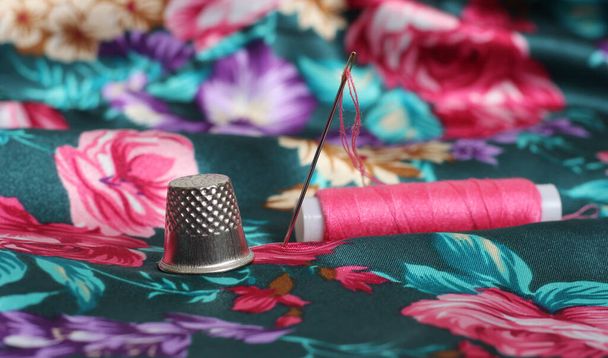 Náprstek s jehlou a růžovou nití na ročníku květinové saténové tkaniny zelené a růžové - Fotografie, Obrázek