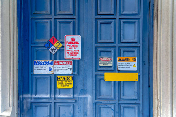 Puerta delantera azul con letreros de advertencia en la parte delantera en San Francisco, California. Diferentes tipos de señales de advertencia en la parte delantera de una puerta doble con marco de puerta de hormigón. - Foto, Imagen