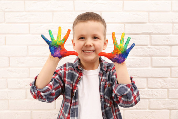 Happy little boy showing painted palms near white brick wall - Foto, afbeelding