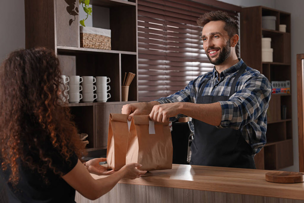 Worker giving paper bags to customer in cafe - Fotografie, Obrázek