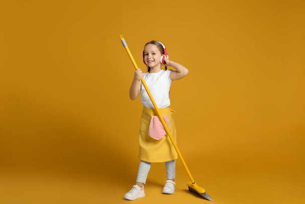 Cute little girl in headphones with broom on orange background - Fotó, kép