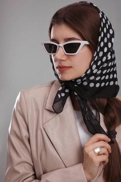 Young woman with sunglasses and stylish bandana on grey background - Valokuva, kuva