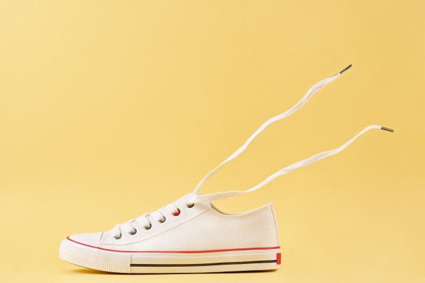 Witte casual sneakers op gele achtergrond, creatief minimalisme - Foto, afbeelding