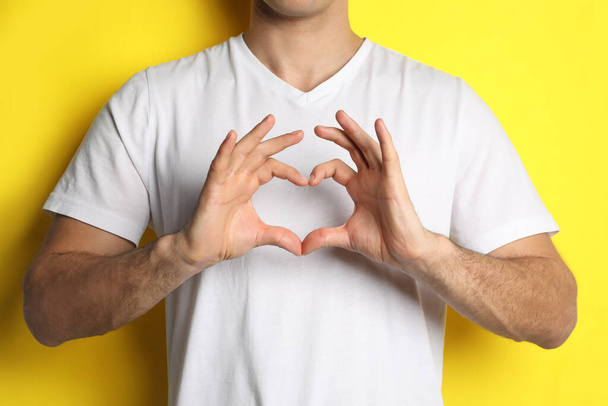 Man making heart with hands on yellow background, closeup - Fotoğraf, Görsel