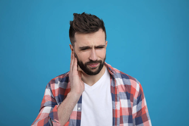 Man suffering from ear pain on light blue background - Foto, Imagen