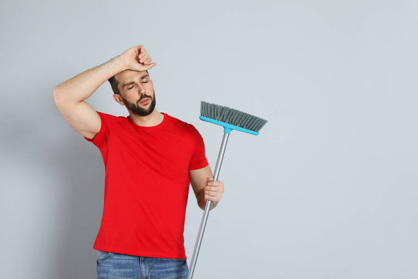 Tired man with broom on grey background, space for text - Fotografie, Obrázek