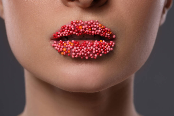 Young woman with beautiful lips covered confectionery sprinkles on gray background, closeup - Valokuva, kuva