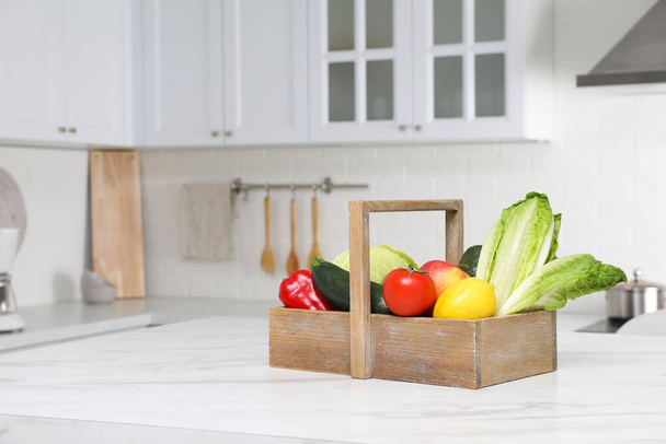 Wooden crate with fresh ripe vegetables and fruits on white table in kitchen, space for text - Foto, imagen