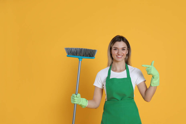 Young woman with broom on orange background, space for text - Фото, изображение