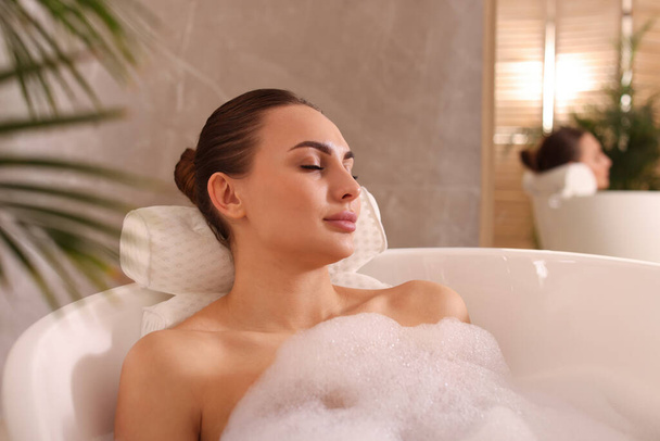 Young woman using pillow while enjoying bubble bath indoors - Valokuva, kuva