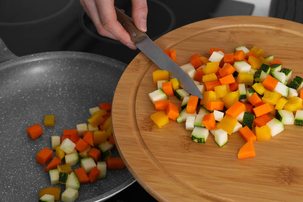 Woman putting cut vegetables onto frying pan in kitchen, closeup - Fotó, kép