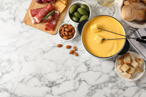 Pot of tasty cheese fondue and snacks on white marble table, flat lay. Space for text - Φωτογραφία, εικόνα