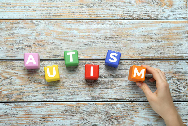 Woman making word Autism with colorful cubes on light wooden table, top view - Photo, Image