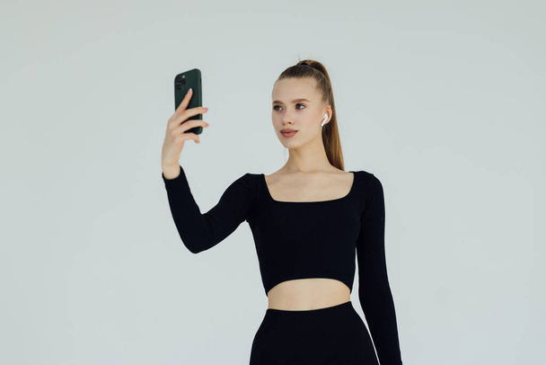 Young woman making video call and pointing gladly at camera of her phone, isolated over white background - Fotografie, Obrázek