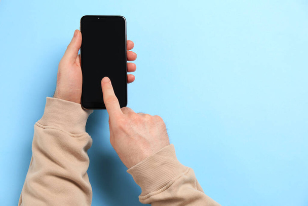 Man using smartphone on light blue background, top view. Space for text - Fotó, kép