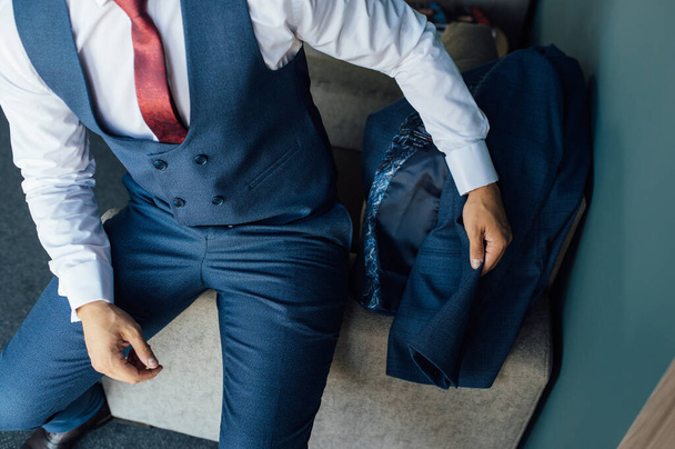 A young businessman in a blue suit takes the suit in his hand and puts it on - 写真・画像