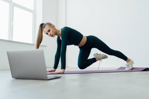 Active fit sporty young woman exercise in living room at home on mat watching online video training tutorial sport live stream workout class on laptop - Foto, Imagem