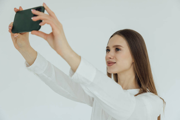 Портрет улыбающейся женщины, делающей селфи с мобильным телефоном на белом фоне - Фото, изображение
