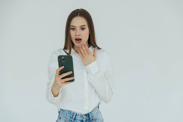Portrait of a shocked woman using mobile phone isolated over white background - Photo, Image