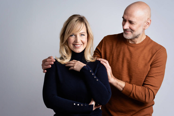Studio shot of a happy middle aged couple standing together at isolated background with copy space. Happy mand embraching beautiful blond haired woman.  - Foto, Imagem