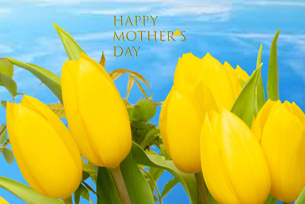 Mothers day greeting card. Decorative composition of a bunch of yellow tulips over abstract blue cloudy sky background with Happy mother's Day text. - Foto, Imagem
