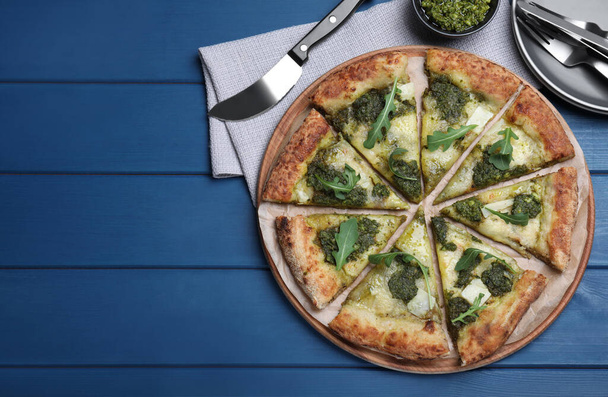 Delicious pizza with pesto, cheese and arugula served on blue wooden table, flat lay. Space for text - Foto, immagini