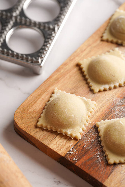 Freshly made traditional italian dish - ravioli, dumplings stuffed with minced meat, on wooden board with flour, aluminum form for preparation - Photo, image