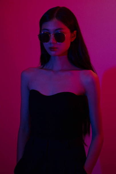 Mode- und Schönheitskonzept: Modefrau trägt Sonnenbrille, um auf Neonlicht-Hintergrund zu posieren. - Foto, Bild