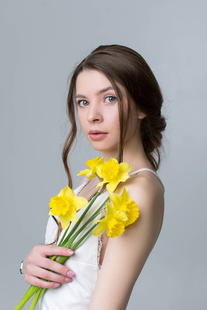 Closeup portrait of beautiful young girl holding yellow flowers in studio - 写真・画像