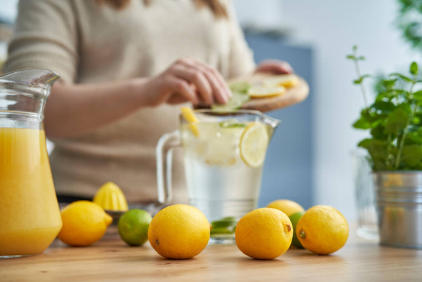 Citrons au premier plan et personne méconnaissable faire de la limonade maison avec du frais  - Photo, image