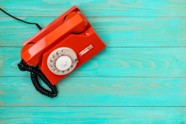 Old, orange rotary dial telephone on blue wooden background. Communication concept. - 写真・画像