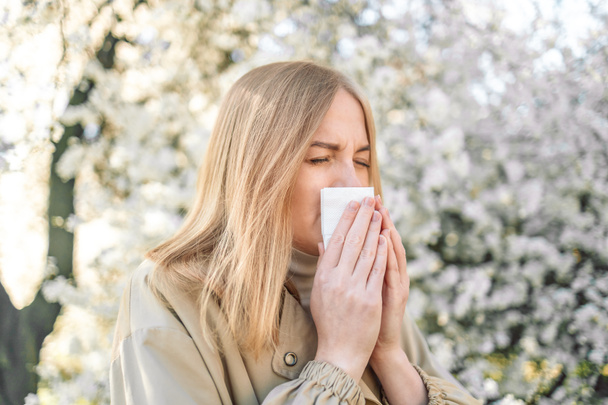 Młoda kobieta z kichającą chusteczką z powodu wiosennej alergii na pyłki. Koncepcja alergii - Zdjęcie, obraz