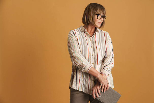 Senior woman wearing eyeglasses posing with planner isolated over beige wall - Photo, image