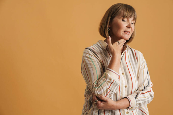 Senior woman wearing striped shirt posing and looking aside isolated over beige wall - Foto, afbeelding
