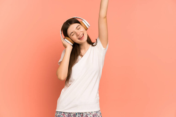 Young Ukrainian girl isolated on pink background in pajamas and holding a pillow and listening music - Photo, Image