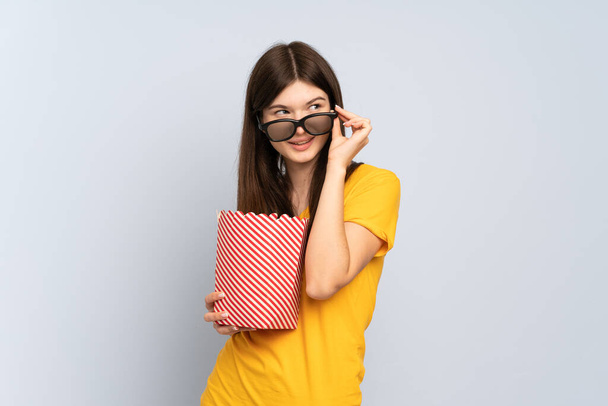 Young Ukrainian girl isolated on white background with 3d glasses and holding a big bucket of popcorns - Foto, imagen