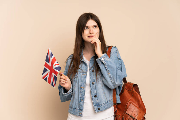 Junge Ukrainerin mit einer britischen Flagge auf beigem Hintergrund, die Zweifel hat und nachdenkt - Foto, Bild